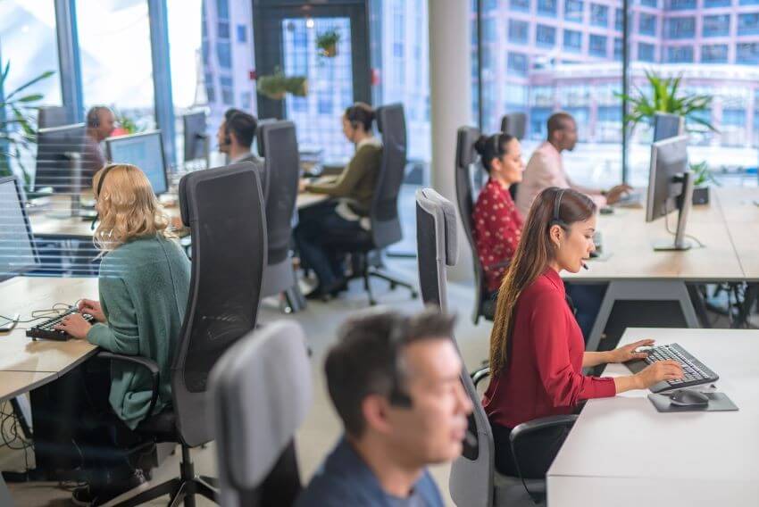 Divers employés d’un centre d’appels travaillant dans un bureau avec des ordinateurs dotés de casques.