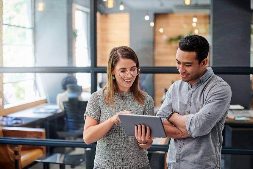 Male and female employees in an office setting looking at a computer tablet that has training and onboarding materials displayed.