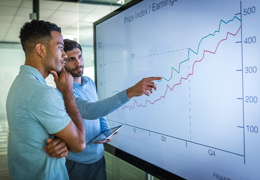 Two businessmen look at a graph on a tv screen