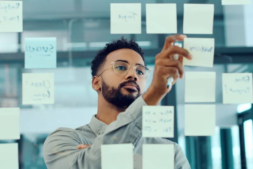 Creative man looking intently at a sticky-note board to solve a business problem in his marketing department