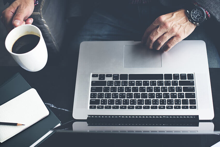 Person using a computer holding a cup of coffee. Aston Carter Recruitment Articles.