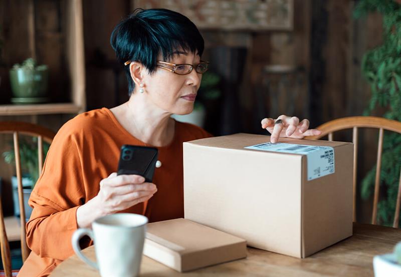 Woman examines a package while sitting at a kitchen table