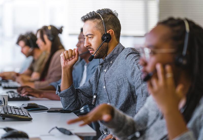Workers sit at a desk taking calls on headsets