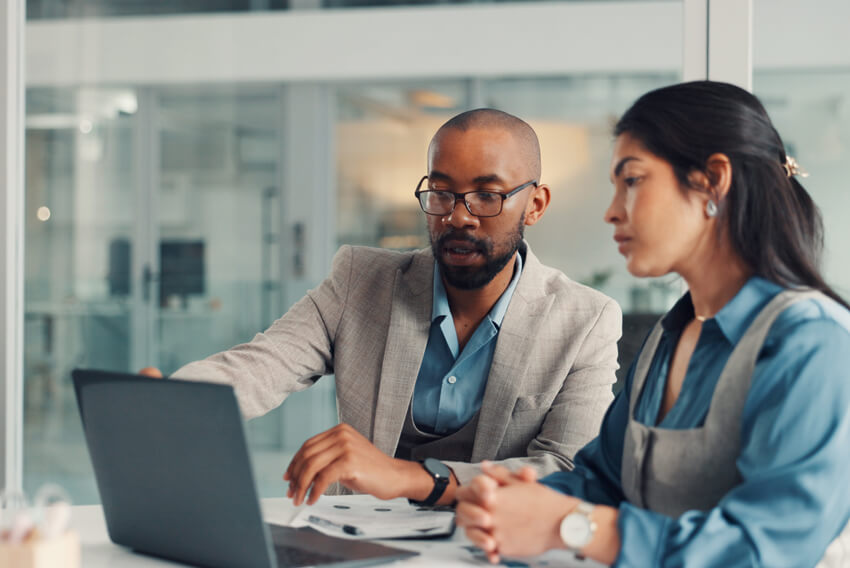 Male and female coworkers reviewing the June 2026 jobs report on a laptop looking at May labor market and economy trends.