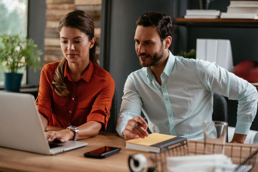 Male and female coworkers reviewing the September 2025 jobs report on a laptop looking at August 2025 labor market and economy trends.