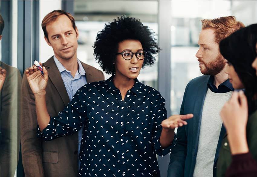 African-American woman writing on a white board, explaining the current labor market to four attentive colleagues.